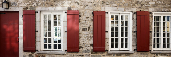 Facade of an old stone house with window and brown shutters. Panoramic image	