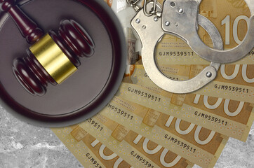 100 Canadian dollars bills and judge hammer with police handcuffs on court desk. Concept of...