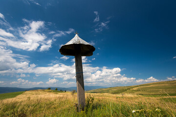 Simple wooden catholic cross on the top of a hill in Transylvania, Romania, beautiful blue sky with white clouds in the background.