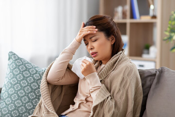 health, cold and people concept - sad sick young asian woman with paper tissue having headache at home