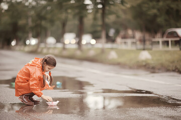 girl plays in paper boats in a puddle / autumn walk in the park, a child plays in the rain