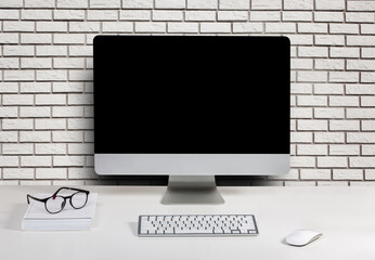 computer display for mockup in office interior on brick wall background. Work desk with keyboard, mouse, glasses, book.