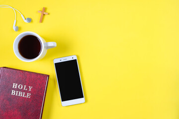Top view of Holy Bible, phone, and a cup of coffee on yellow background