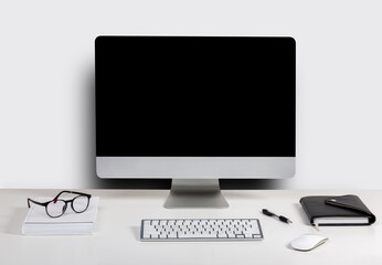Isolated computer display for mockup in office interior. Work desk with keyboard, mouse, book, glasses, Free space on wall for text.