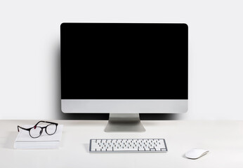 Isolated computer display for mockup in office interior. Work desk with keyboard, mouse, book, glasses, Free space on wall for text.