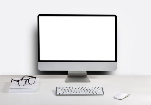Isolated computer display for mockup in office interior. Work desk with keyboard, mouse, book, glasses, Free space on wall for text.