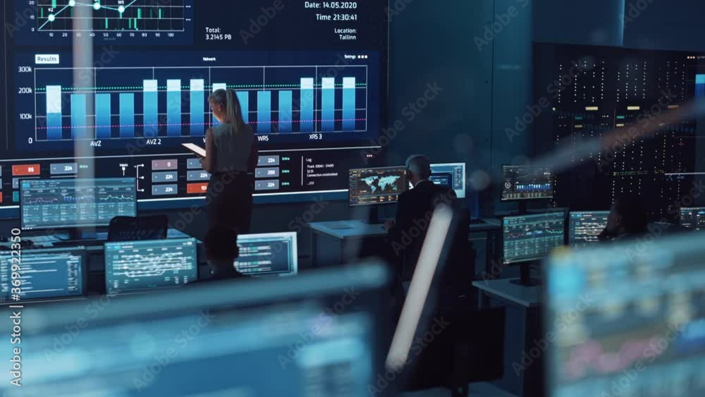 Poster Software Engineers Working in a Room with a Big Screen in a Modern Monitoring Office with Live Analysis Feed with Charts. Monitoring Room Big Data Scientists and Managers Sit in Front of Computers.