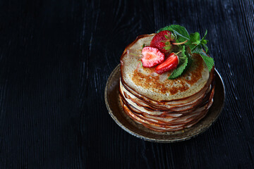 A stack of pancakes with strawberries and mint . Photo on a black background. Copy of the space.Top view.