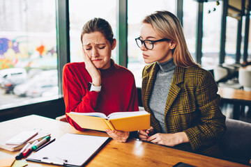 Frustrated intelligent student crying because of done stupid mistake in course work.Confused hipster girl has problem reading literature textbook and preparing for exam together with private teacher