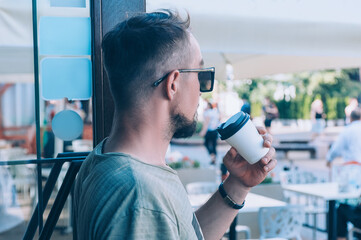 The guy is drinking coffee in a plastic cup at a cafe.
