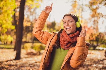 Can not be bothered. Photo of pretty careless dreamy lady smiling close eyes listen music fingers up dancing autumn park wear headphones scarf green turtleneck orange windbreaker outside