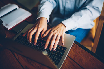Cropped image of female hands typing text on keyboard of modern laptop computer device connected to...