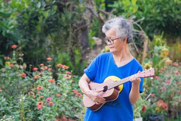 Portrait of an elderly woman holding ukulele while standing in a garden