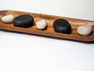 Massage white and black stones on a wooden tray in white background. Spa stones use for wellness treatment and relaxation. Space for text