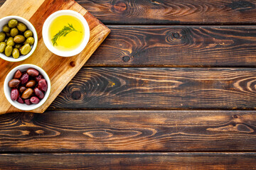 Green and black olives, olive oil in bowls on cutting board top-down copy space