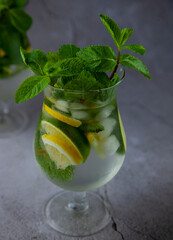 Summer mint lime refreshing cocktail mojito with rum and ice in glass on gray background. Mojito cocktail on stone table. Glassy high glass for drinks. Lemonade at the bar.
