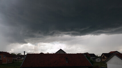 Dark ominous storm clouds followed by heavy rain over the roofs of houses in the suburban settlement of Bosanski Brod, Bosnia and Herzegovina.