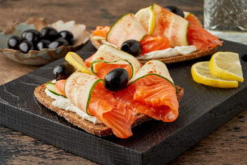 Smorrebrod - traditional Danish sandwiches. Black rye bread with salmon, cream cheese, cucumber and olives on dark brown wooden background