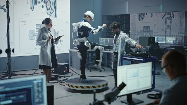 In Robotics Development Laboratory: Engineers and Scientists Work on a Bionics Exoskeleton Prototype with Person Testing it. Designing Wearable Exosuit to Help Disabled People, Warehouse Workers
