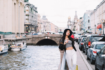 Half length portrait of beautiful female tourist standing on the background of wonderful buildings in the city, fashionable hipster model having a good time during evening walk in the urban setting