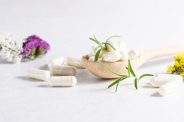 Collagen capsules for skin and beauty in the wooden spoon with herbs and flowers on white marble table close up. Health care concept.