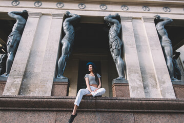 Full length portrait of admirable and fashionable hipster girl sitting in front of the ancient...