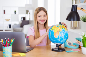 Photo of positive girl child sit table desk study remote use globe want explore earth continent in house indoors