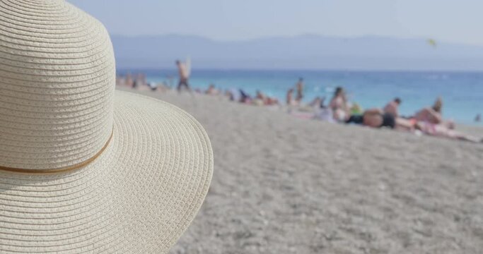 A woman with a hat is sitting on the beach. She keeps a social distance because of the corona virus. Famous Golden Horn beach (Zlatni Rat) in Croatia.
