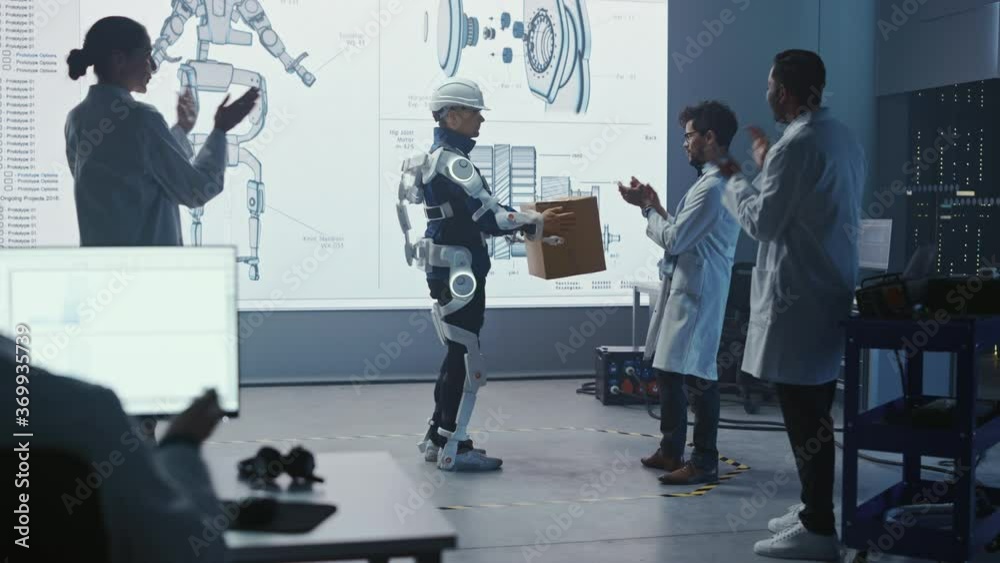 Aufkleber In Development Laboratory: Engineers and Scientists Look at Robotics Exoskeleton Presentation with Person Lifting Heavy Carboard Box, People Applaud and Celebrate After Successful Testing