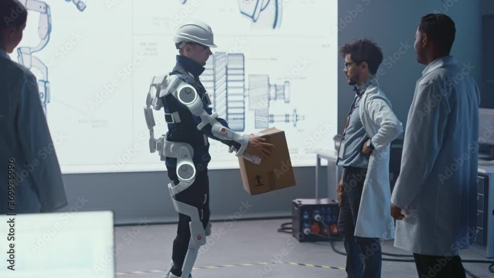 Poster In Development Laboratory: Engineers Look at Robotics Exoskeleton Prototype Presentation with Person Testing it, Lifting Heavy Carboard Box. Designing Wearable Exosuit to Help Warehouse Workers