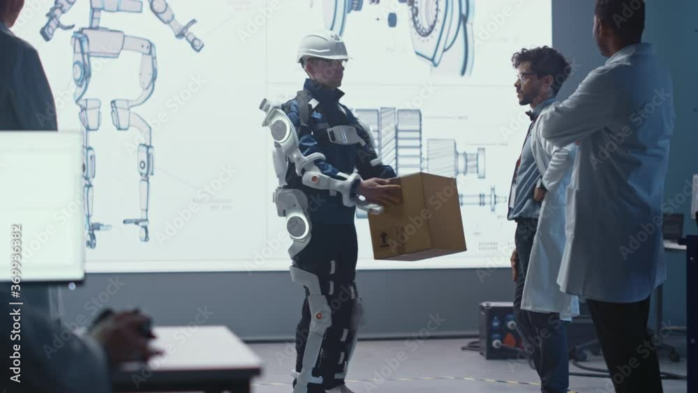 Poster In Development Laboratory: Engineers Look at Robotics Exoskeleton Prototype Presentation with Person Testing it, Lifting Heavy Carboard Box. Designing Wearable Exosuit to Help Warehouse Workers