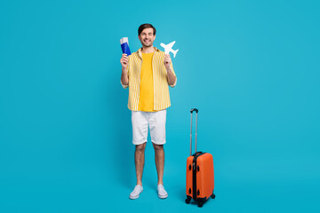 Full size photo of positive man enjoy traveling hold tickets paper card plane have luggage for check-in verification wear good look outfit isolated over blue color background