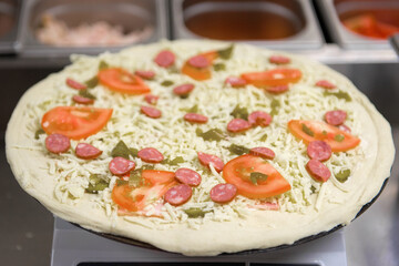 Blank dough for making pizza with sausage and tomatoes on a kitchen scale, close-up.