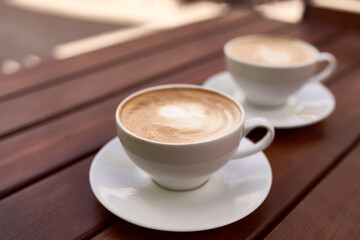 Two cups of cappuccino on the wooden background. Beautiful brown foam, white ceramic cups, place for text