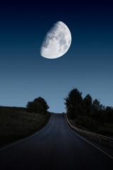 A road leading toward huge and beautiful moon on night sky