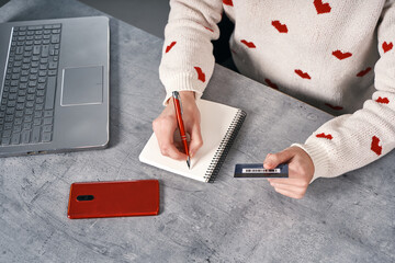 Woman hands writing in notepad and holding bank card. Shopping online concept
