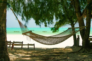 Isolated braided empty beach hammock hanging in shade on trees in caribbean sea island. Tropical summer vibes and mood. Turquoise sea, white sand, blue sky.