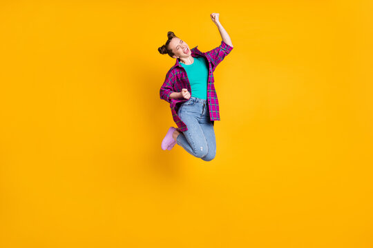 Full Length Profile Photo Of Pretty Crazy Excited Teen Lady Jump Up Support Sports Team Competition Raise Fists Scream Wear Casual Plaid Shirt Sneakers Jeans Isolated Yellow Color Background