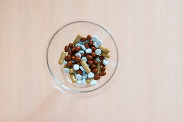 Pills in a glass bowl on a beige background. Top view