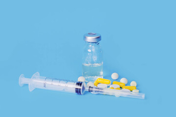 many multicolored pills, syringe and medicine bottle on blue background