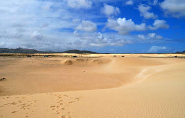 Fototapeta na wymiar Road through the desert, huge sand dunes and beautiful clouds. Dunas de Corralejo, Fuerteventura, Canary Islands