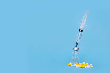 syringe stuck in a vial of medicine and near many multicolored pills isolated on blue background