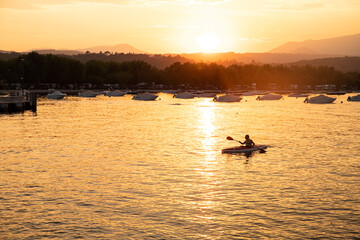 Man not recognizable kayaking in Manerba del Garda waters at sunset. Garda Lake, Italy.