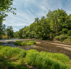 river with weir between forests, blue sky with gathered clouds