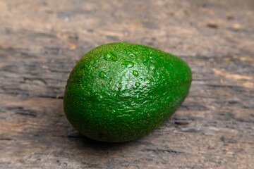 whole fresh avocado in wooden plate on dark wooden table background.