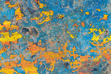 Old concrete wall with remnants of bright paint. Colors - blue, yellow, orange. Peeling, cracking, weathering. 
