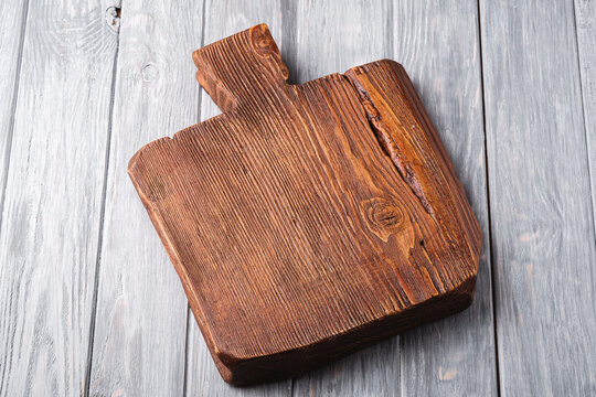 Handcraft dark brown teak wooden old cutting board, grey background, angle view