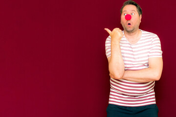 The happy surprised charming trendy and smiling man on red nose day or april fools day.Man shows to the side
