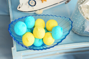 Sweet appetizing bright yellow and blue sugar  in icing sugar in a glass plate on a light, background,close,top view. Round color dessert.Brigth sweet balls.Yellow and blue marshmallows.Candy bar