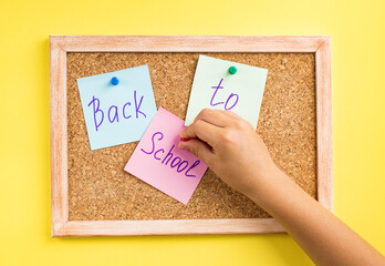 A child's hand attaches colored notes to a cork Board. Yellow background. Let's go back to the...
